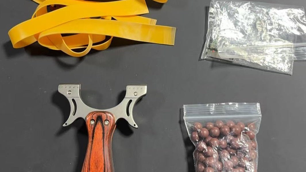 Tirachinas de mango de madera con gomas de repuesto y bolsa de bolas sobre fondo oscuro